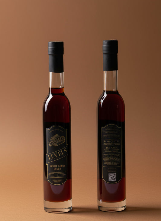 Two bottles of Cassia Burnt Sugar Cocktail Syrup, one standing in front of the other, with labels facing forward on a white background.