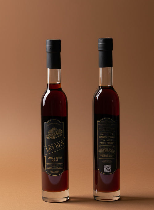 Two bottles of Cassia Burnt Sugar Cocktail Syrup, one standing in front of the other, with labels facing forward on a white background.